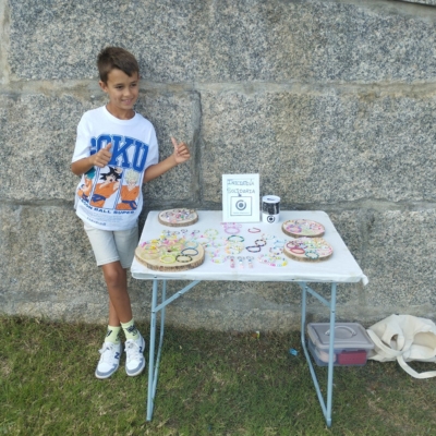 Hugo, de 8 años, junto a su stand solidario de pulseras y llaveros para Objetivo Diagnóstico, sonriendo con los pulgares arriba.